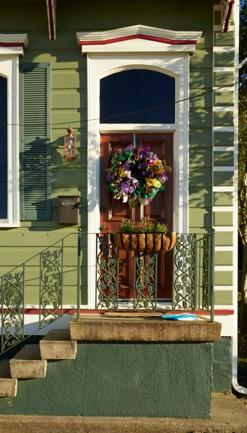 The raised front stoop of a green New Orleans cottage: concrete steps, a decorative iron rail, and a painted masonry base below the front door.